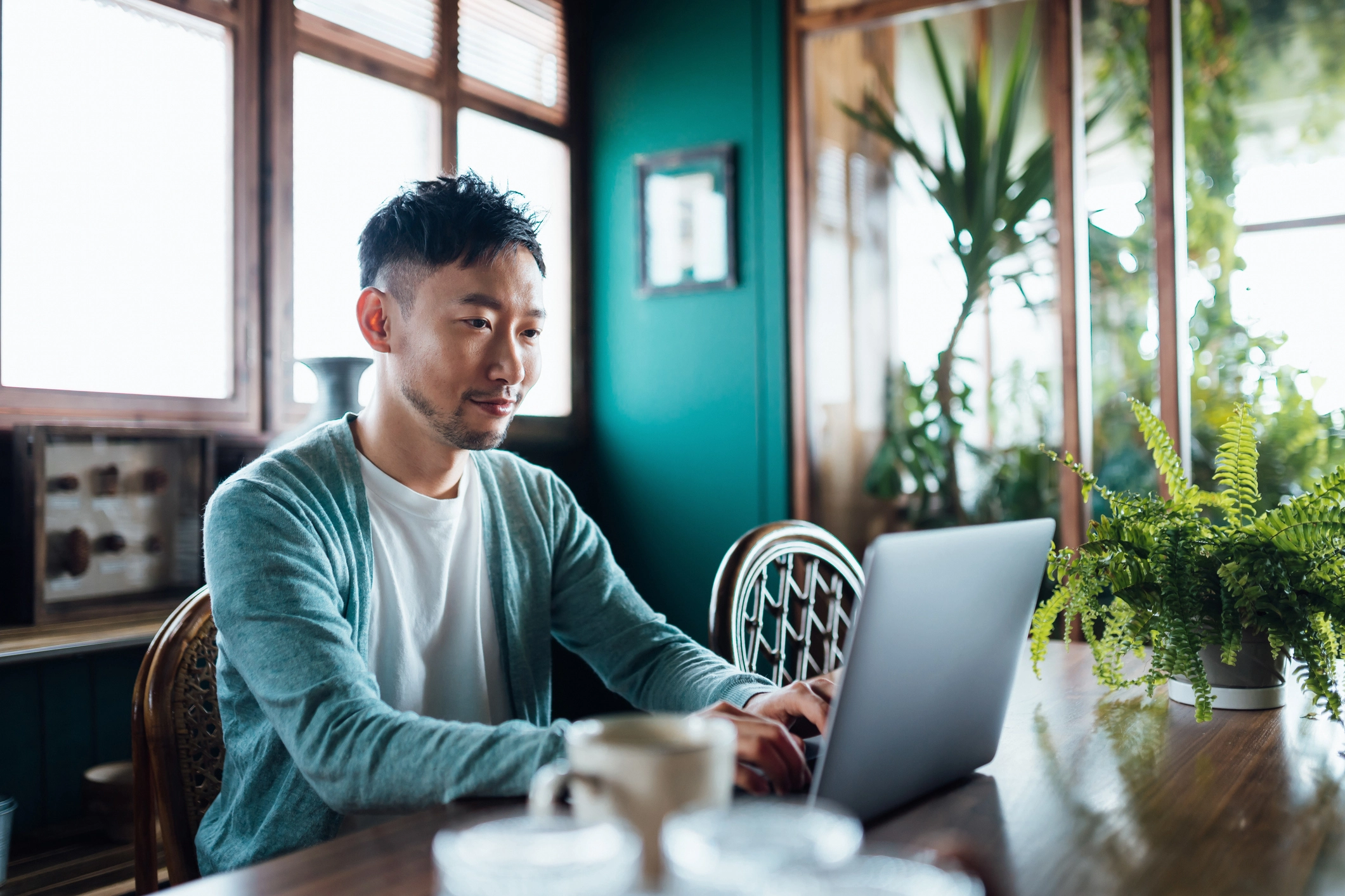 A self-employed professional working on a laptop at a home office, surrounded by plants, symbolizing the flexibility and independence of self-employment