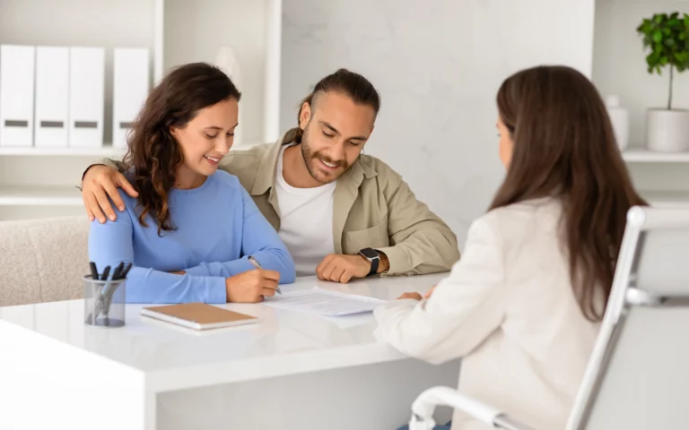 Couple happily signing mortgage refinancing documents with a financial advisor in a modern office setting