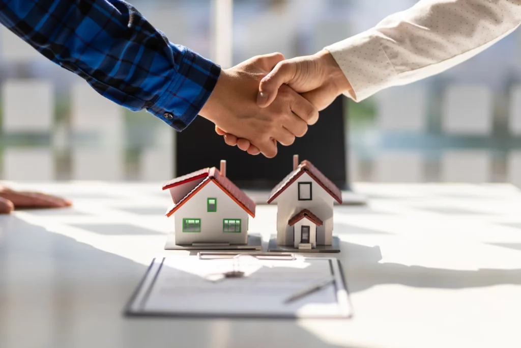 Handshake finalizing real estate agreement with model houses and contract on desk